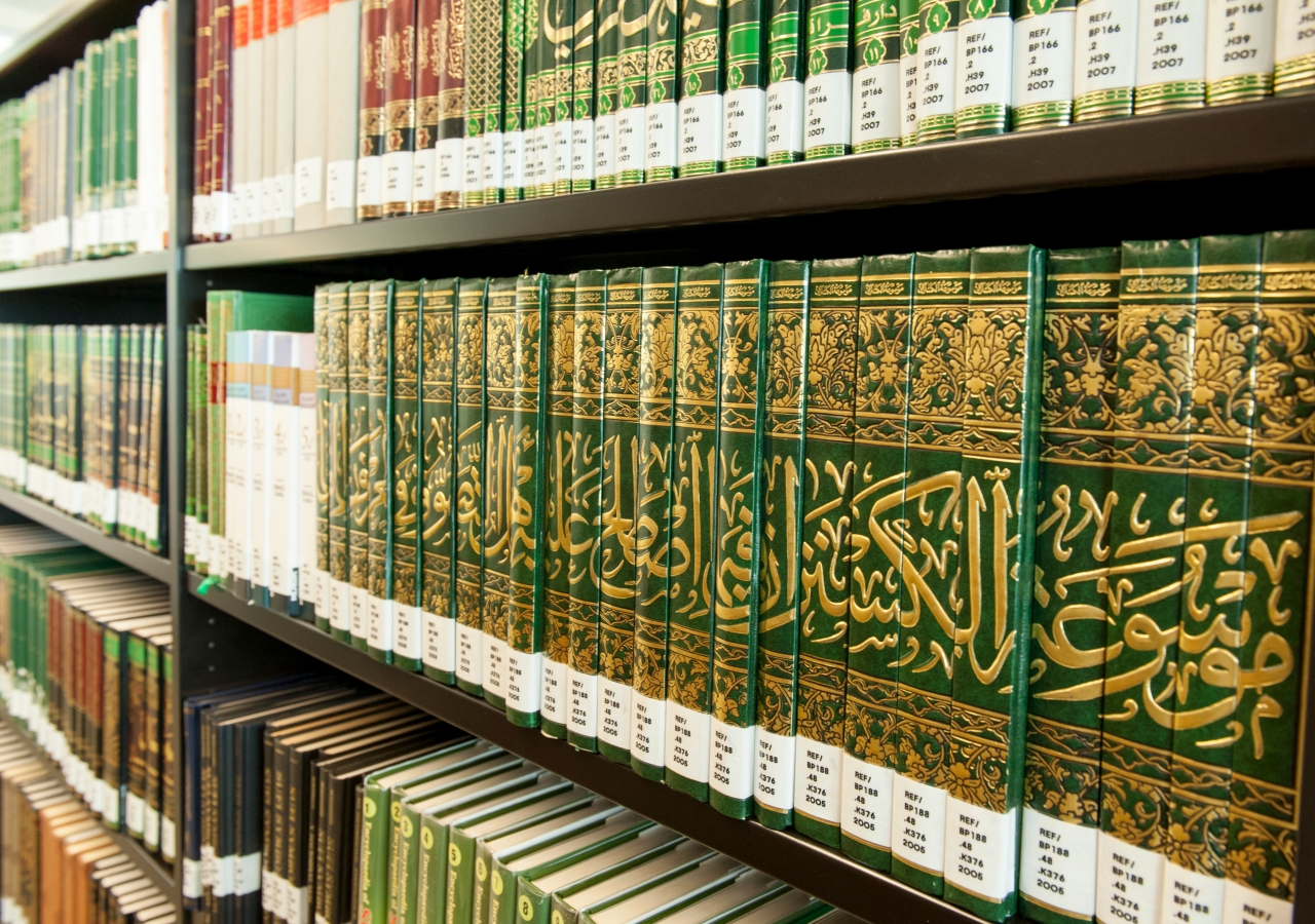 "Bookshelves filled with green and gold Islamic books neatly arranged in a library."